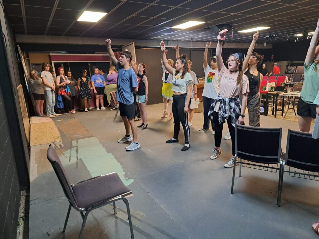 Performers rehearsing with raised arms, simulating excitement over royal ball invitations.