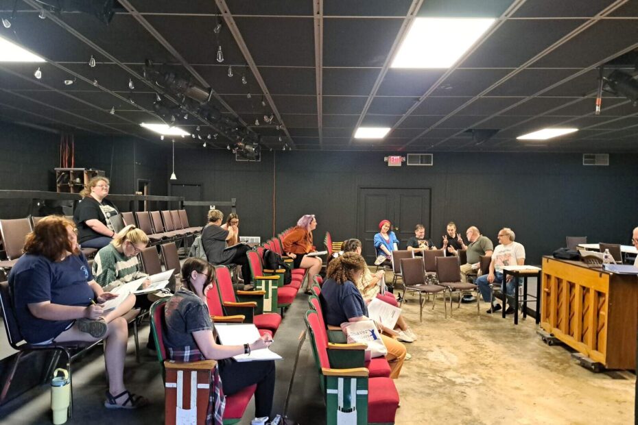 Group of actors and crew seated in a rehearsal space reviewing music and discussing scenes during Week 2 of Cinderella rehearsals.