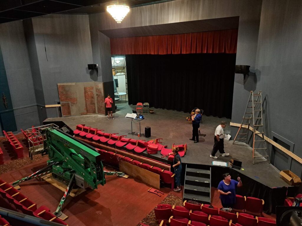A wide-angle view from the balcony shows ongoing stage setup, ladders, and scattered seats in Lyric Theatre.