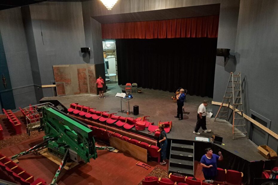 A wide-angle view from the balcony shows ongoing stage setup, ladders, and scattered seats in Lyric Theatre.