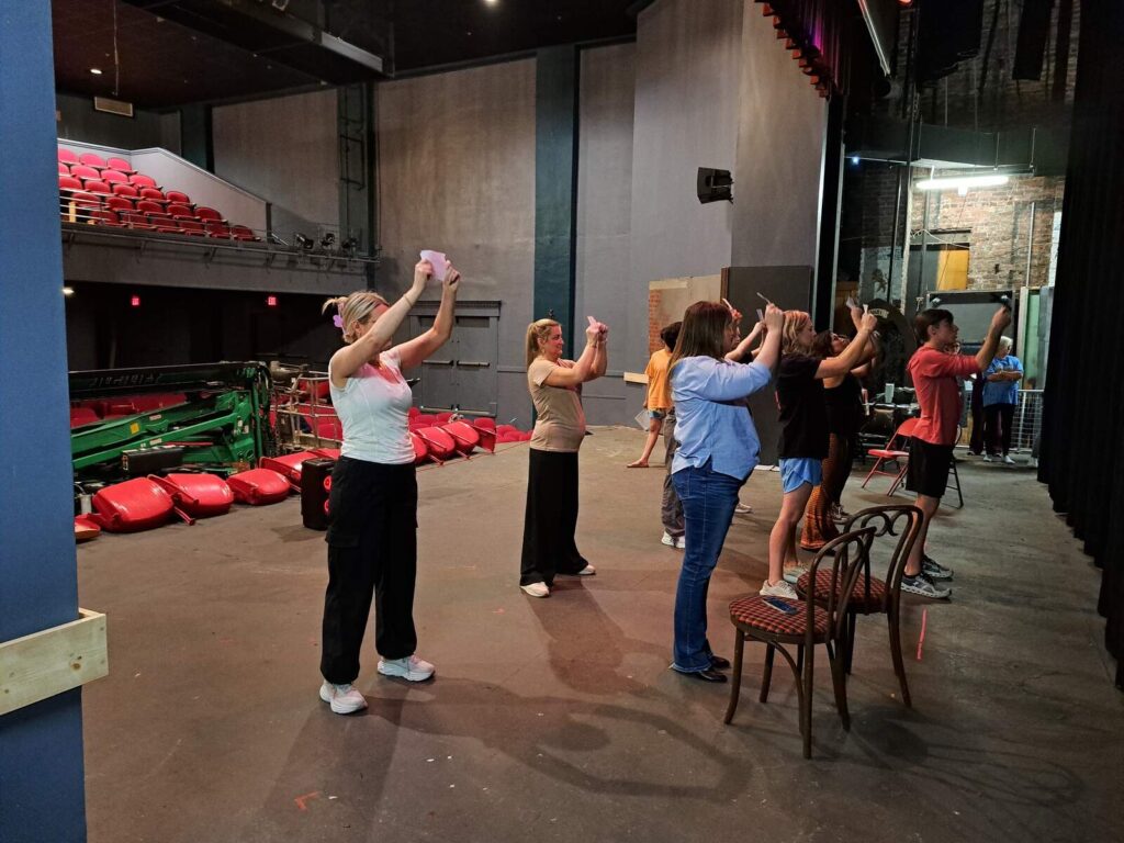 Featured dancers at rehearsal excitedly hold royal invitations overhead at Lyric Theatre