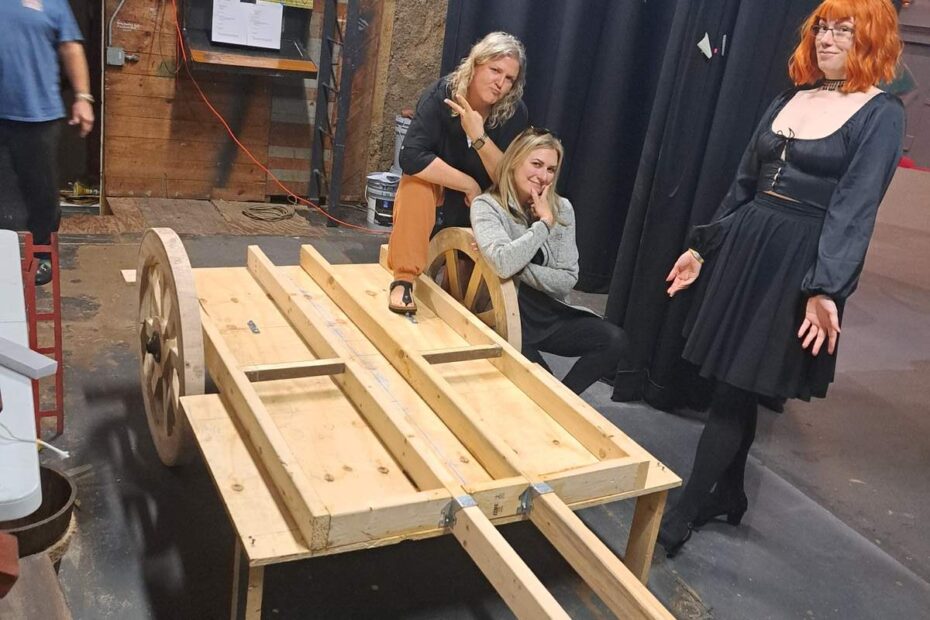 Cast members posing with partially built wooden carriage backstage at Cinderella rehearsals.