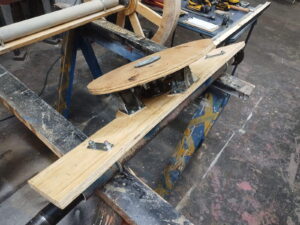 Partially constructed turning mechanism for the front wheels of a stage carriage, made with wood and mounted casters.