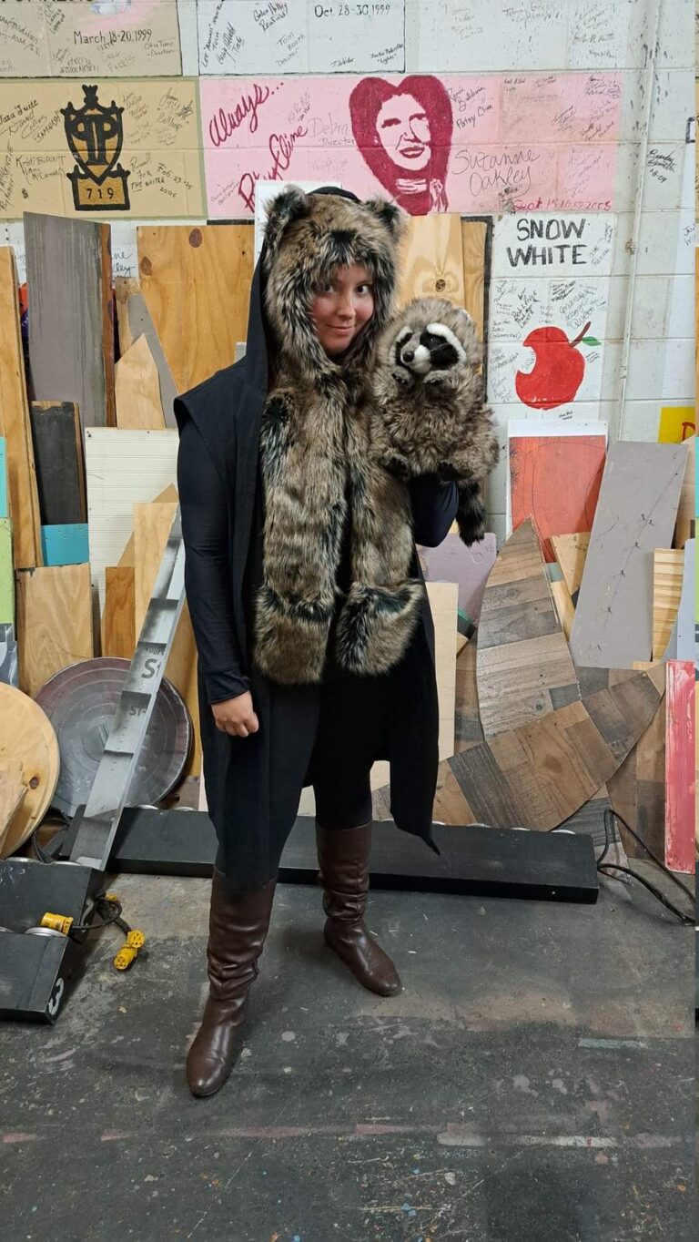 Actor models creature cloak while holding plush raccoon
