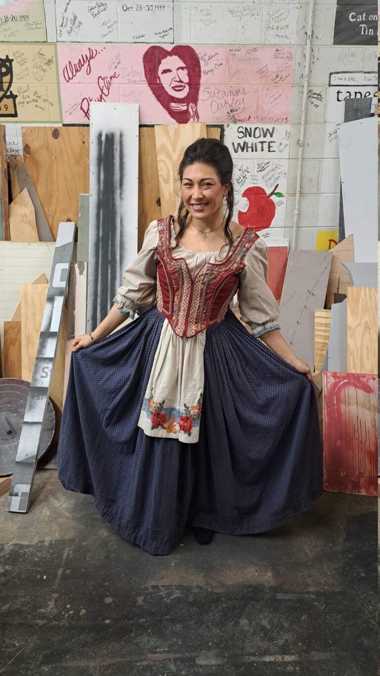 Smiling performer spreads full blue skirt in workshop