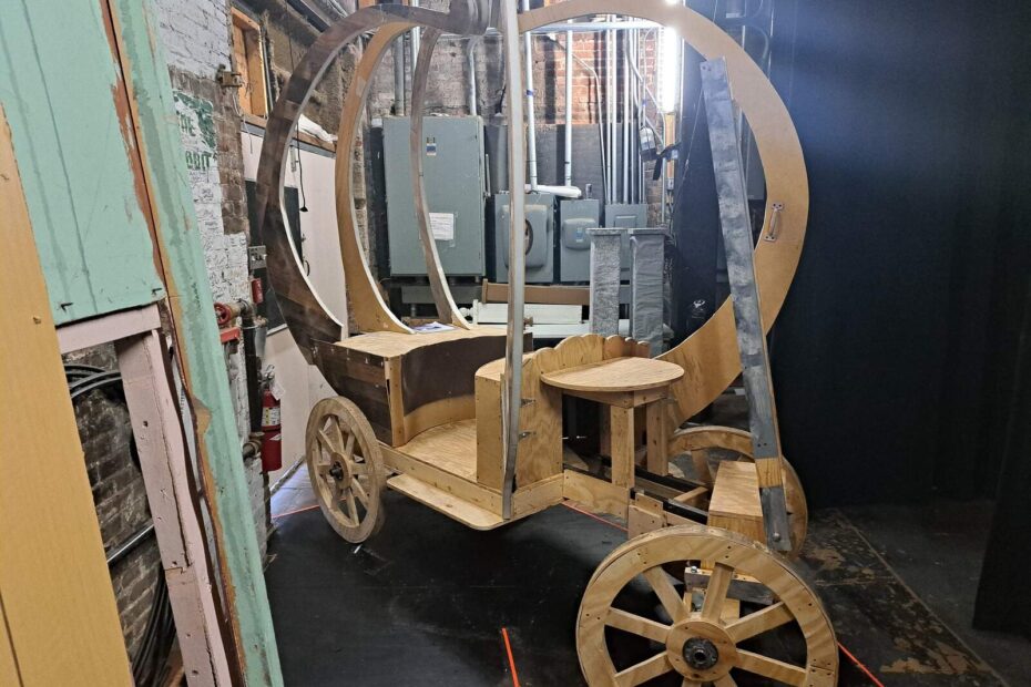 Unpainted wooden carriage frame shaped like a pumpkin rests on sturdy wheels