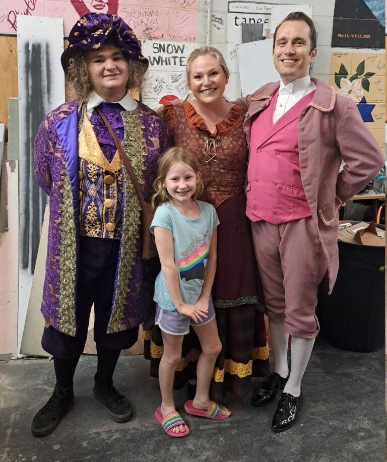 Trio of adults in ornate period dress pose with smiling girl in casual clothes
