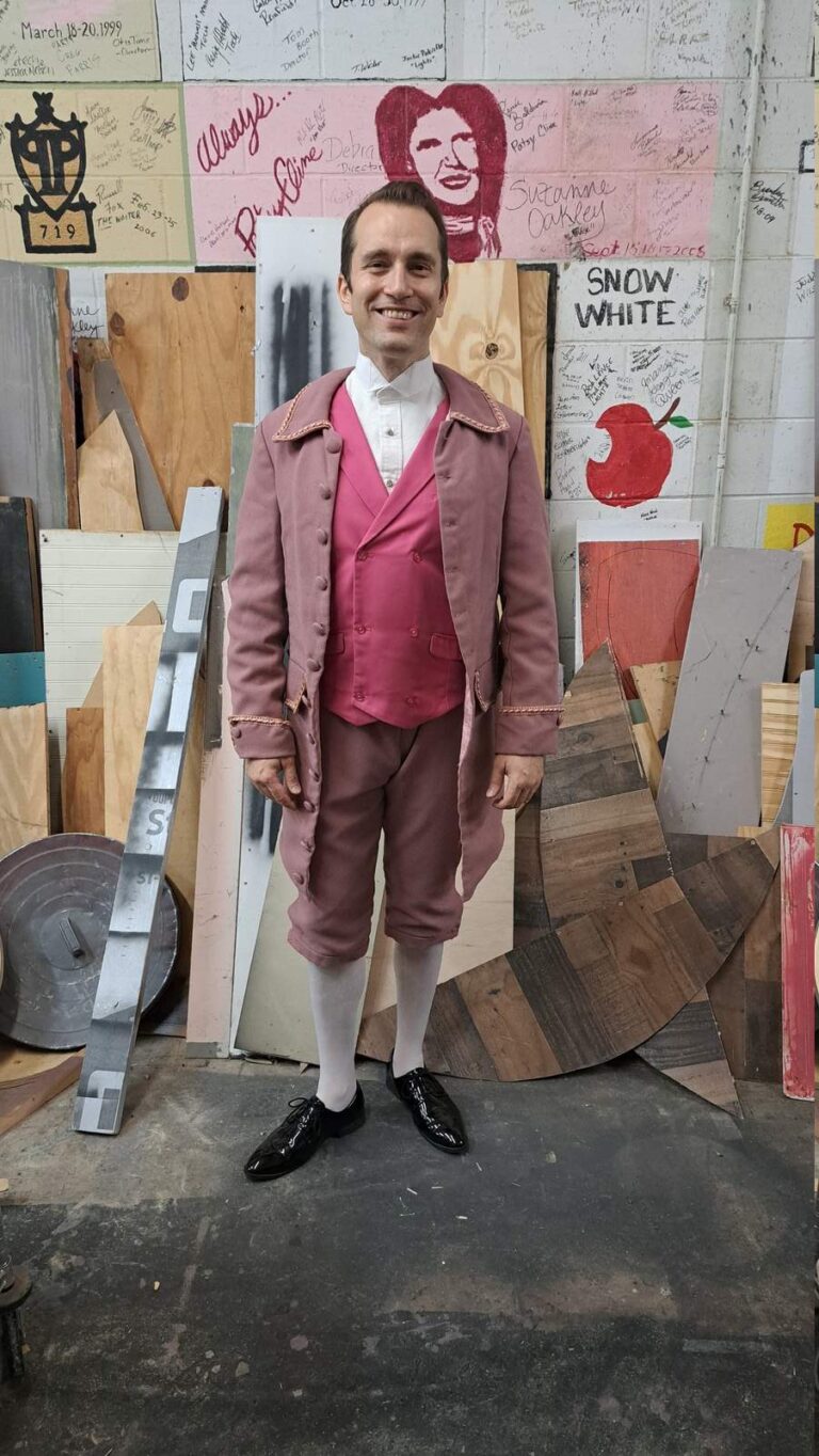 Smiling performer models rose-colored coat with decorative cuffs back stage