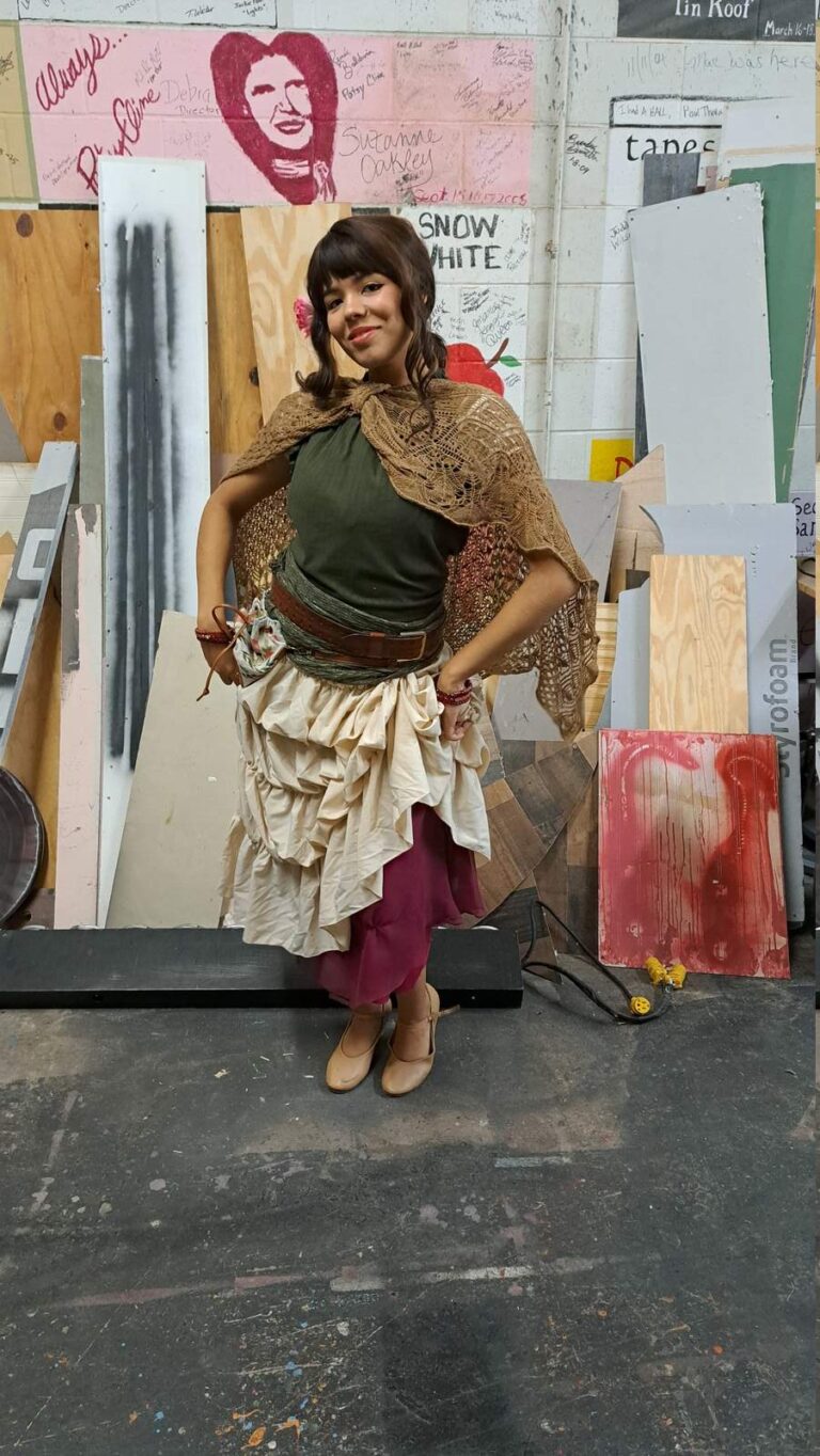 Cast member wears tiered cream skirt, olive blouse, and crocheted shawl backstage