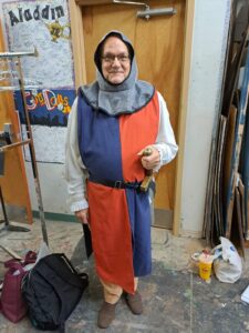 Bobby Geno in red-and-blue tabard with chainmail-style hood holding sword hilt