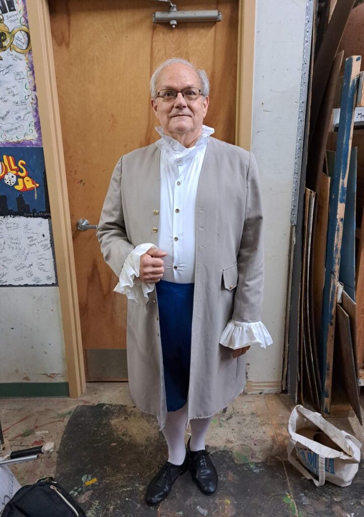 Performer in beige long coat, ruffled cravat and blue breeches