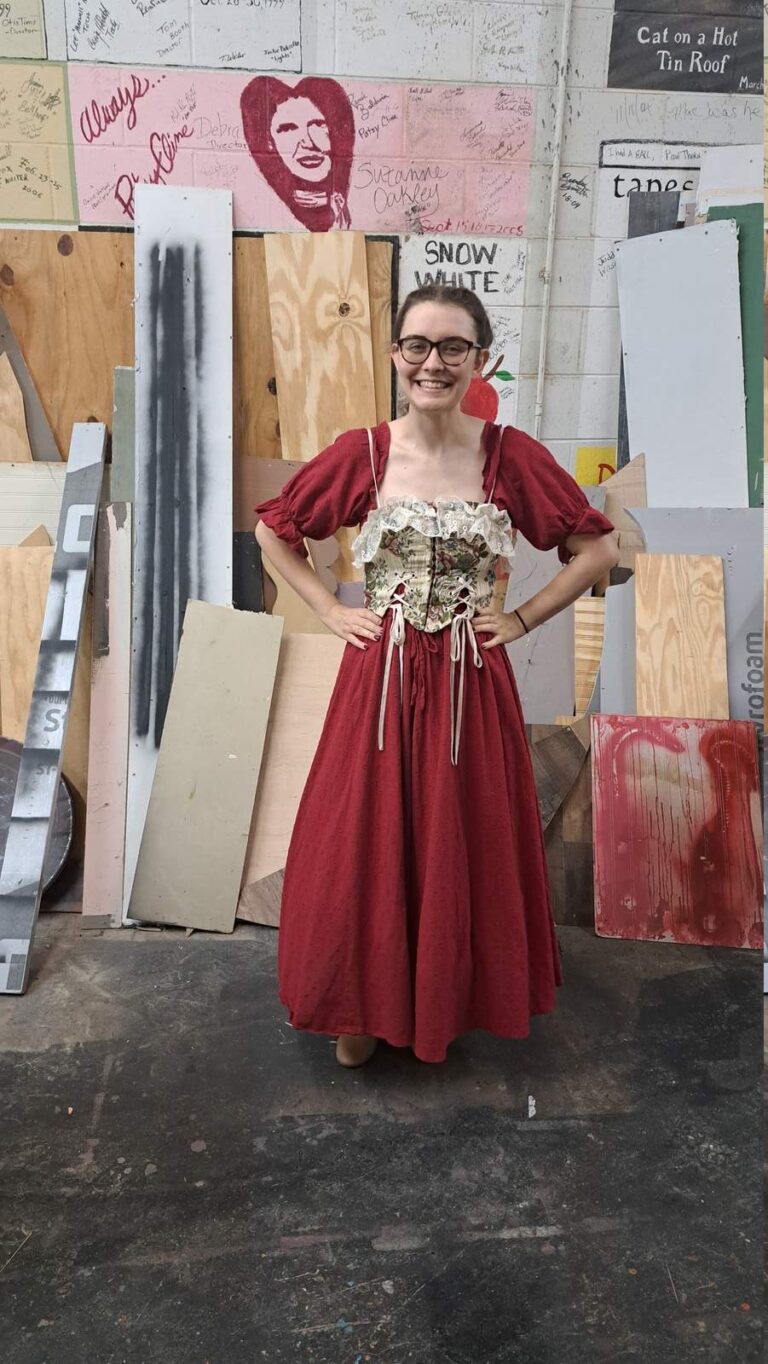 Performer poses in ankle-length red dress with floral lace-up bodice