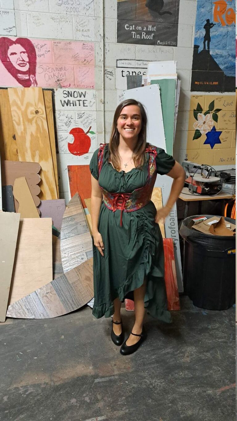 Performer in green ruffled dress with embroidered red corset smiles on set