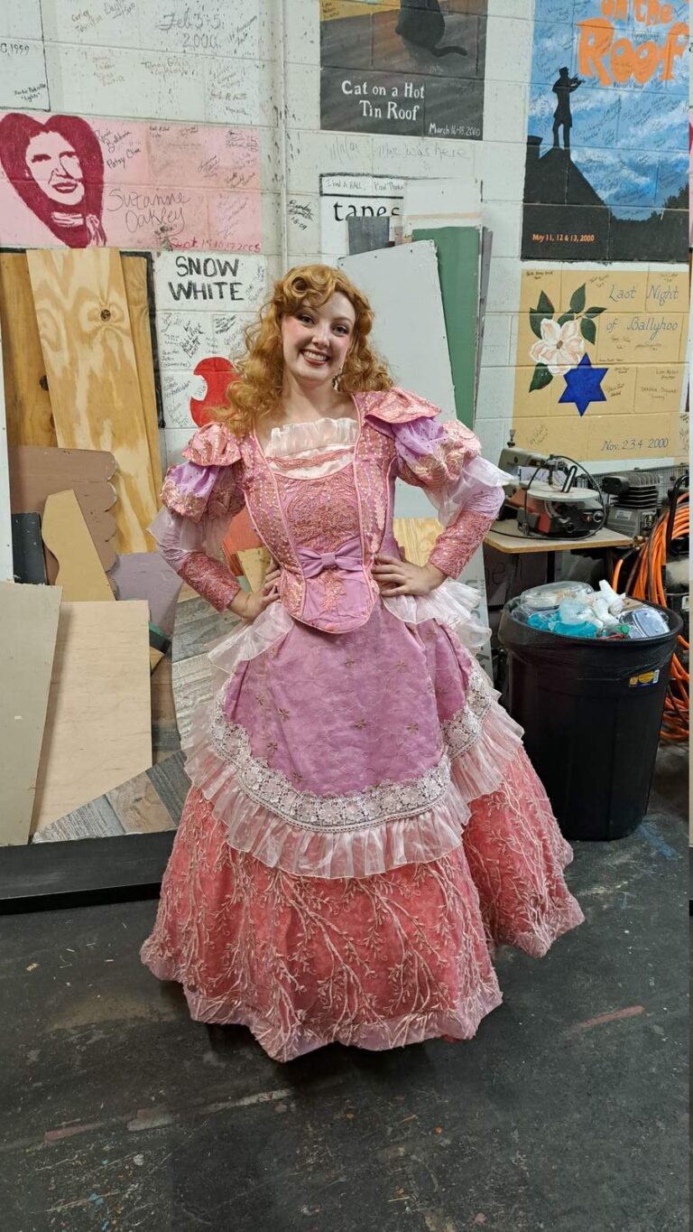 Performer in ornate pink layered gown with ruffles and lace strikes a pose