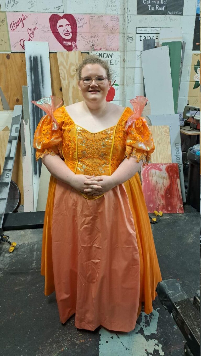 Performer in orange satin gown with embroidered bodice and puff sleeves
