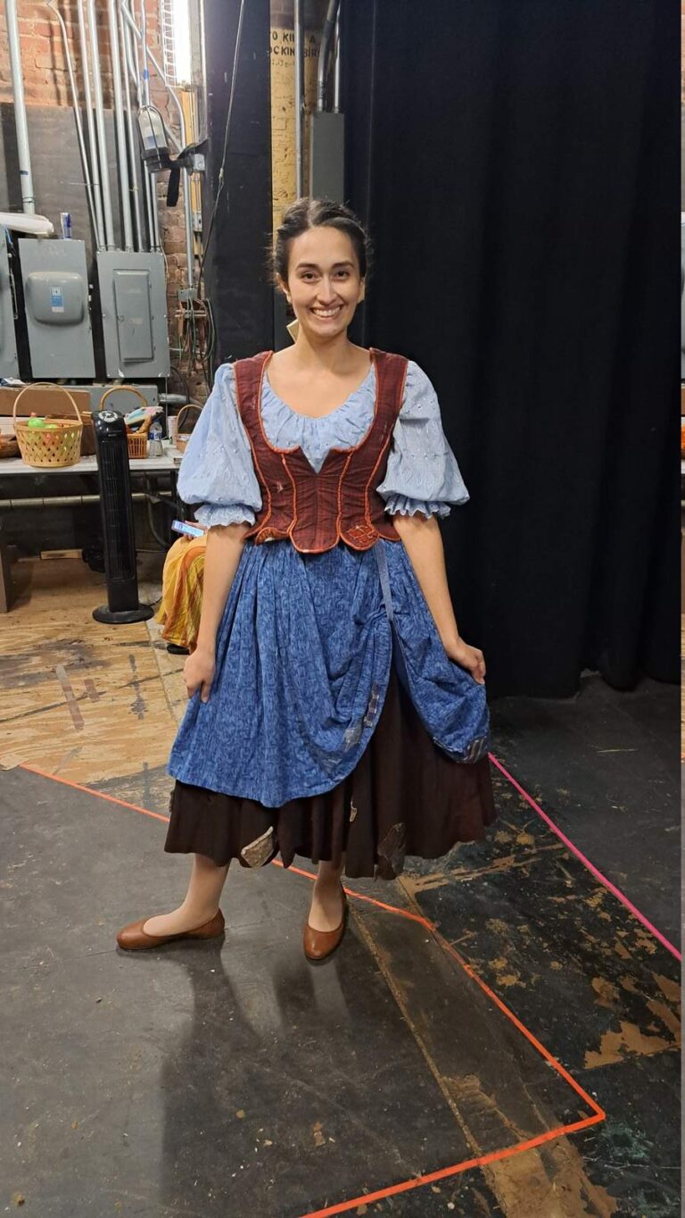 Performer wears blue puff-sleeve dress with rust-brown corset backstage
