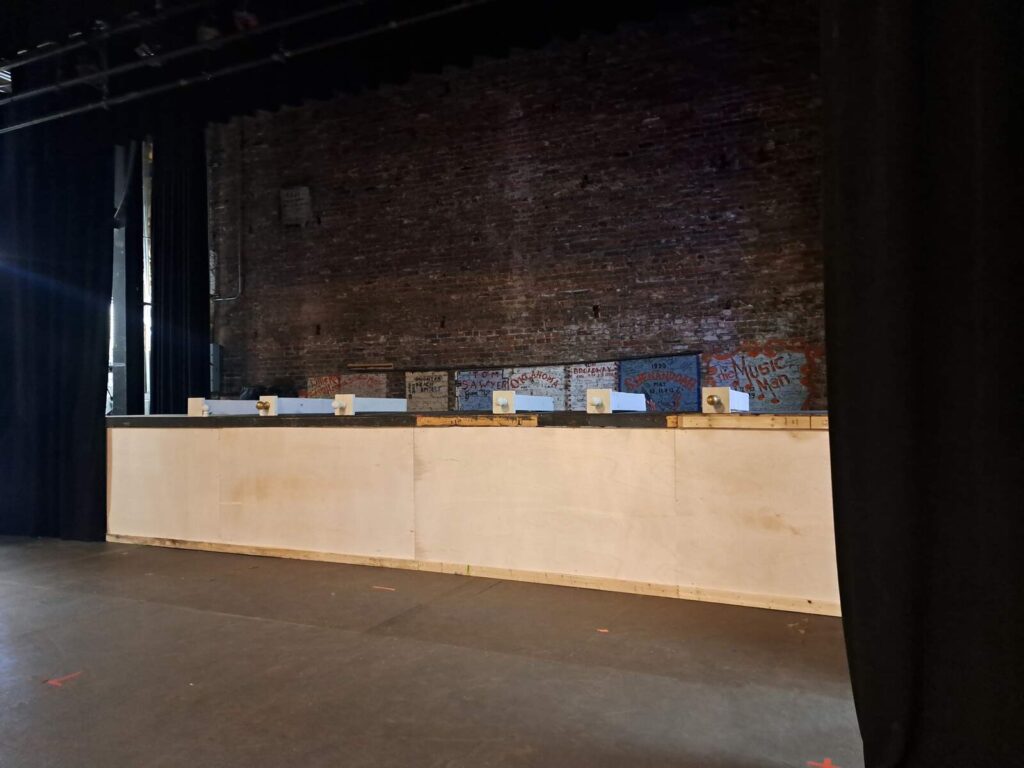 Simple wood structure runs the width of the stage under dim work lights.