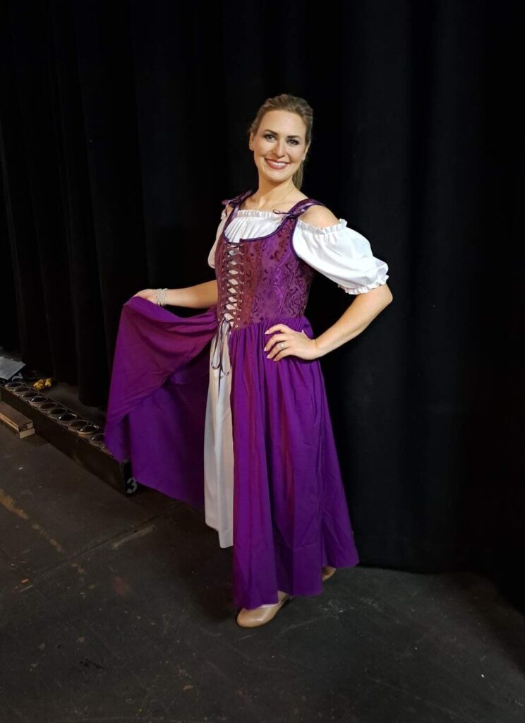 Full-length shot: woman in vibrant purple folk dress holding skirt for dramatic flare.