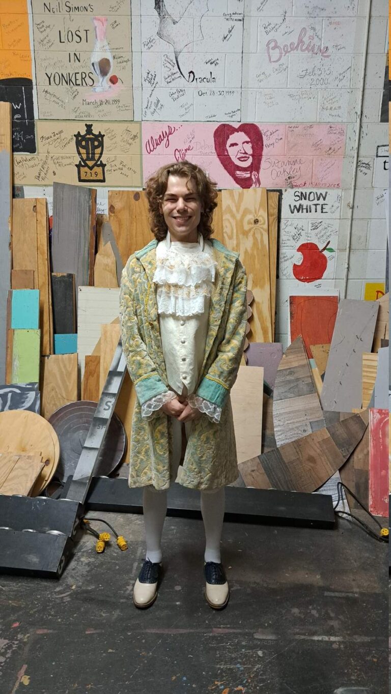 Performer in pale green patterned coat with lace cuffs and cream waistcoat